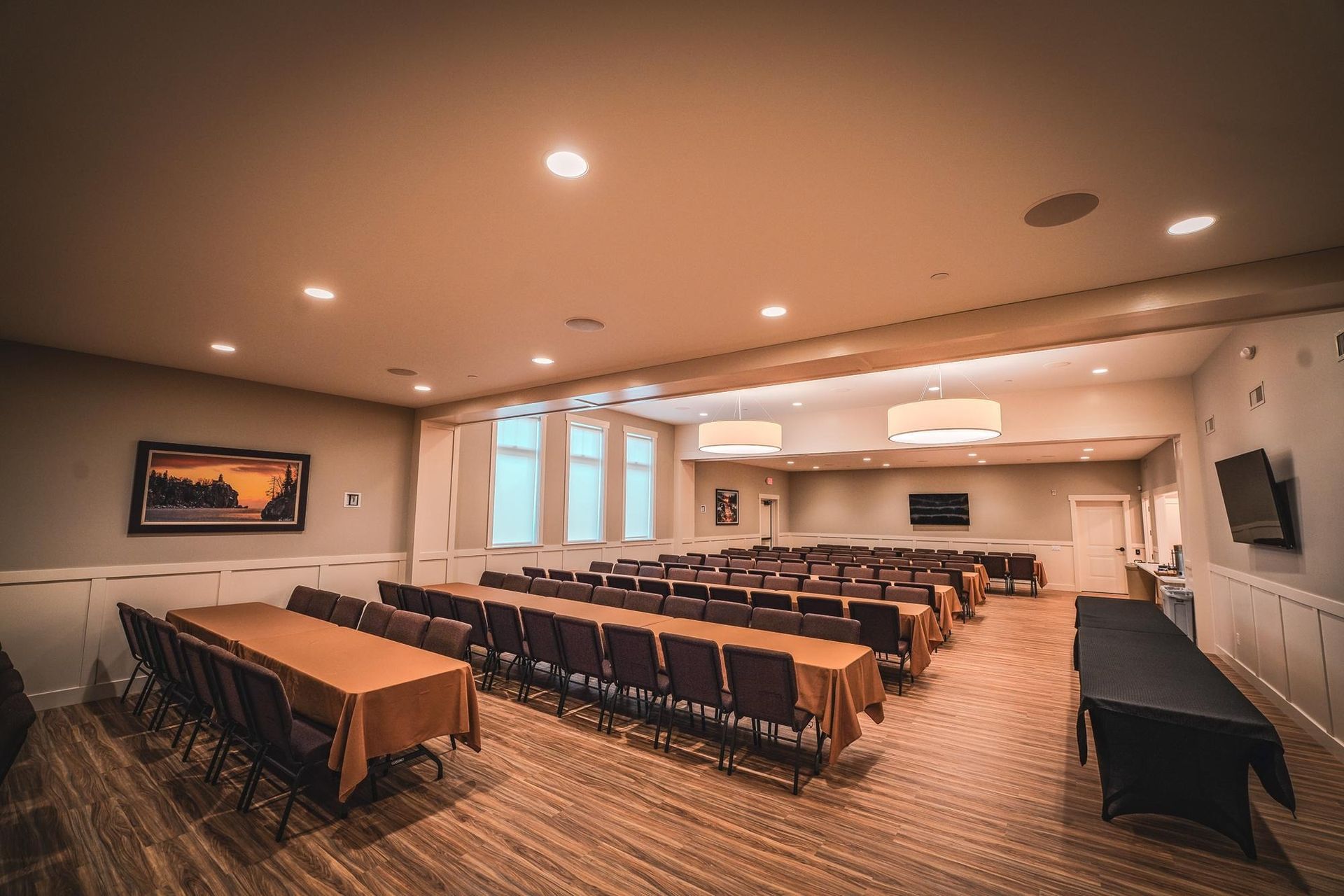 Conference room with rows of chairs facing a table with a black cover. Beige and brown tones.