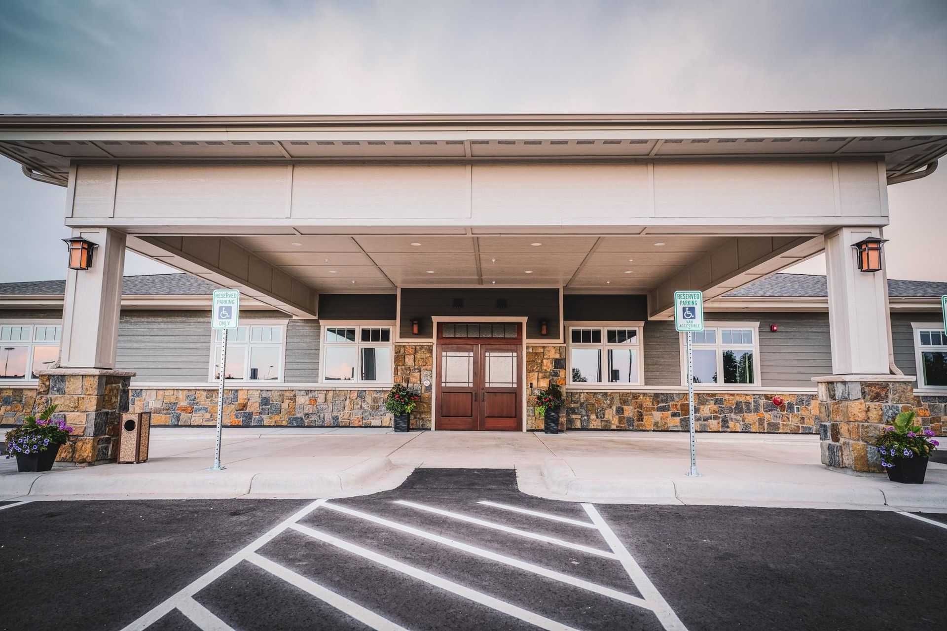 Exterior of a building with a covered entrance, stone facade, and designated parking spots.