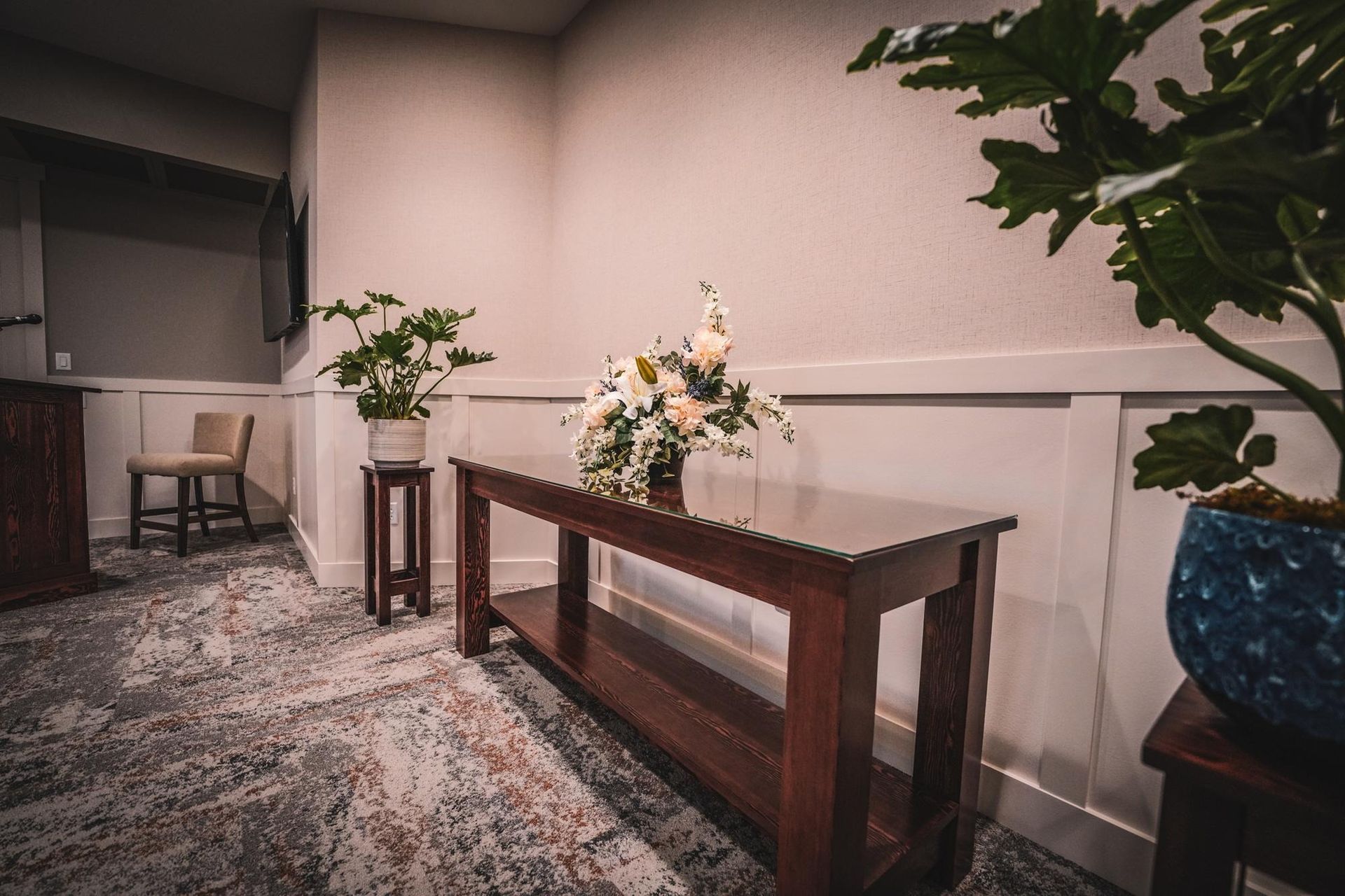 Dark wood table with floral arrangement, potted plants, and chair in a hallway.