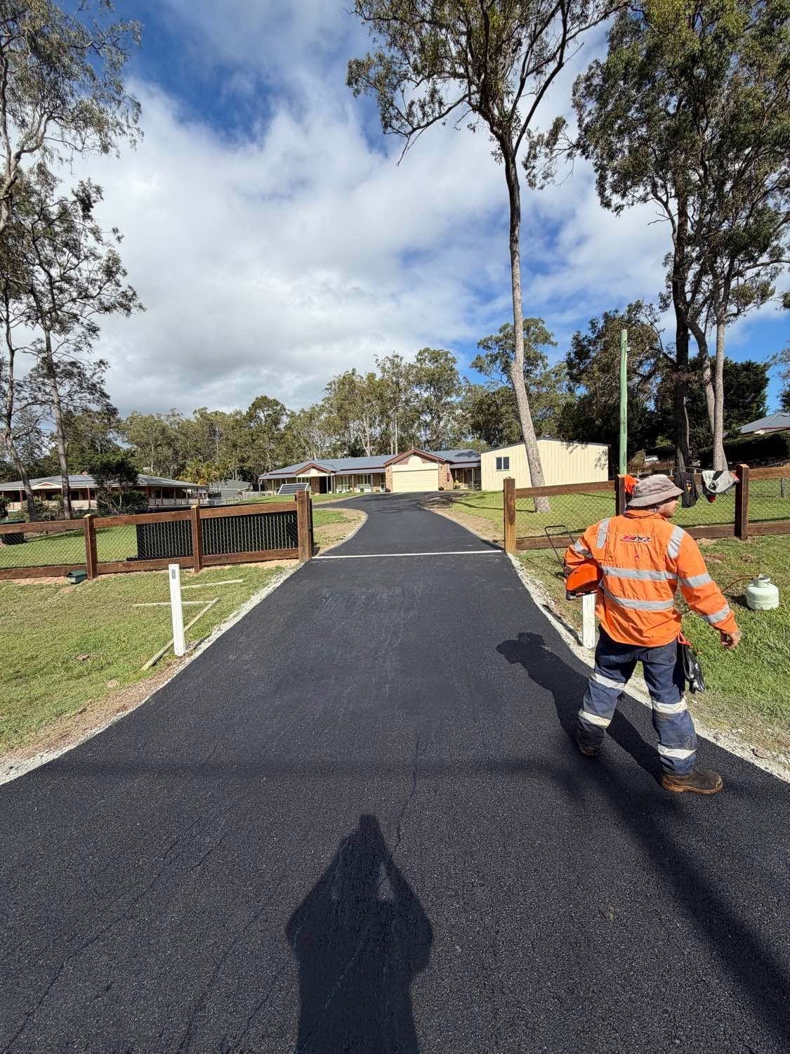 Worker in orange safety vest on a newly paved path near a park playground under a partly cloudy sky