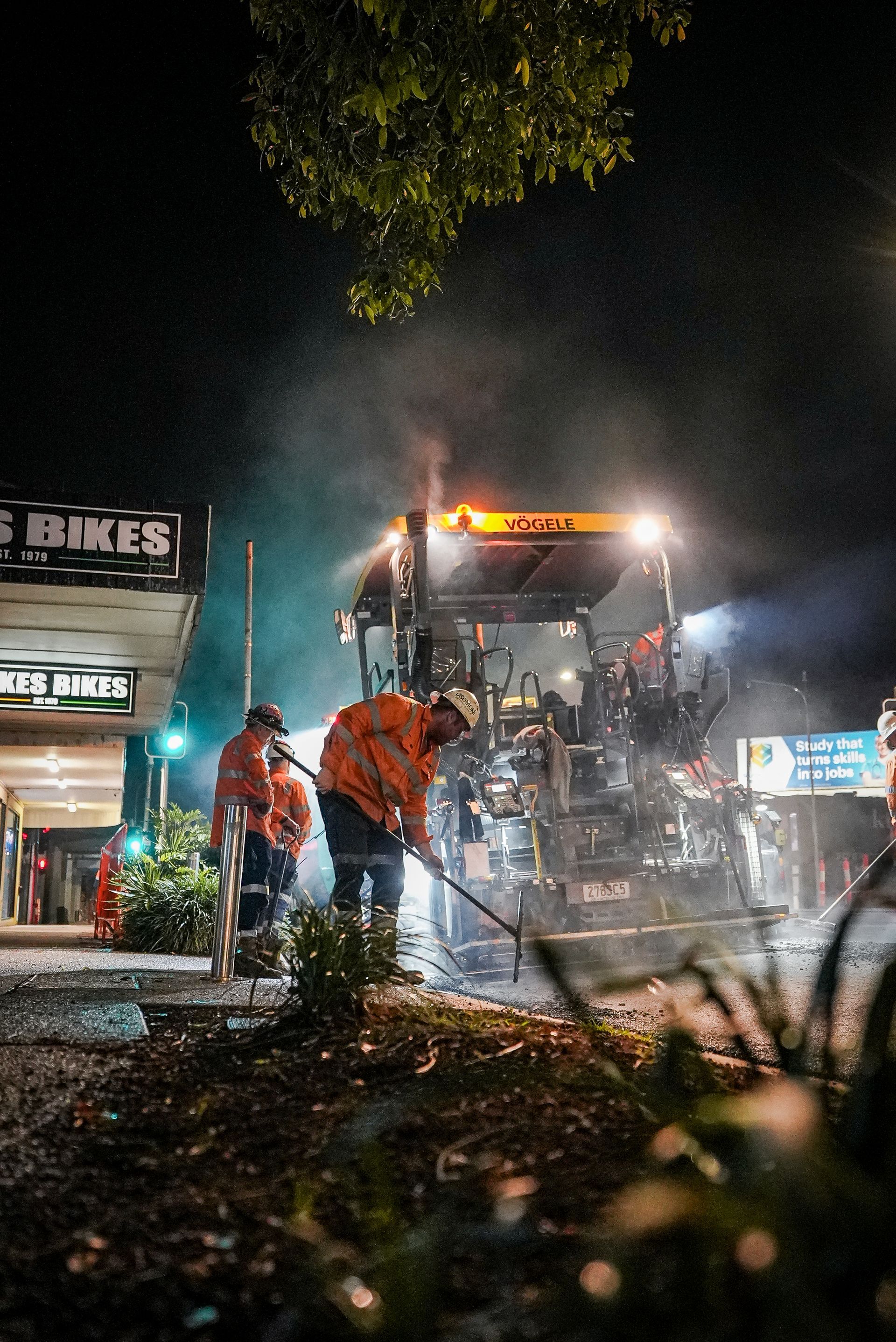 Workers using a hose to extinguish a fire on a wet street at night, with a lit vehicle in the background
