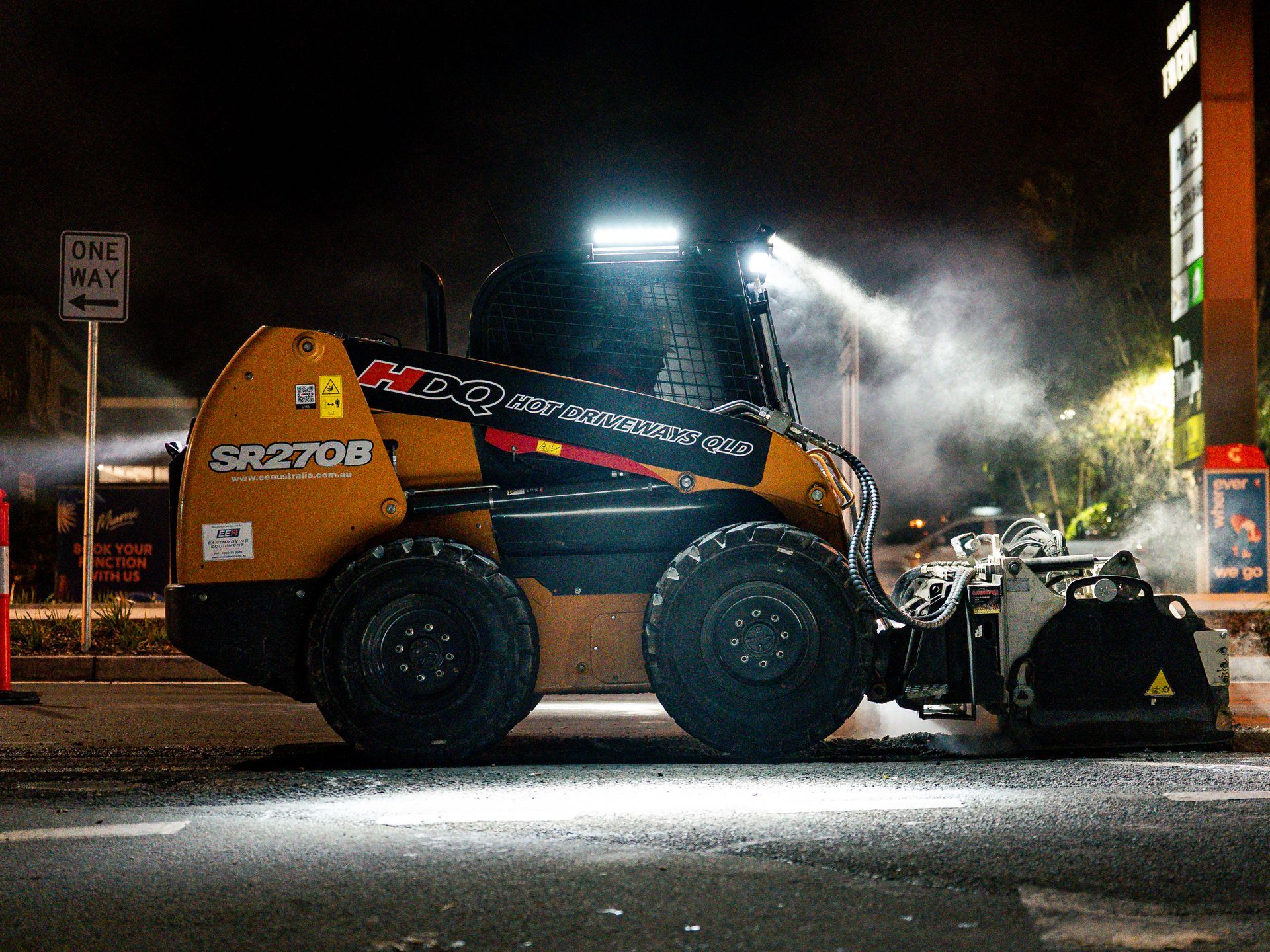 Orange construction vehicle with six wheels operating at night, spraying water beside a road.