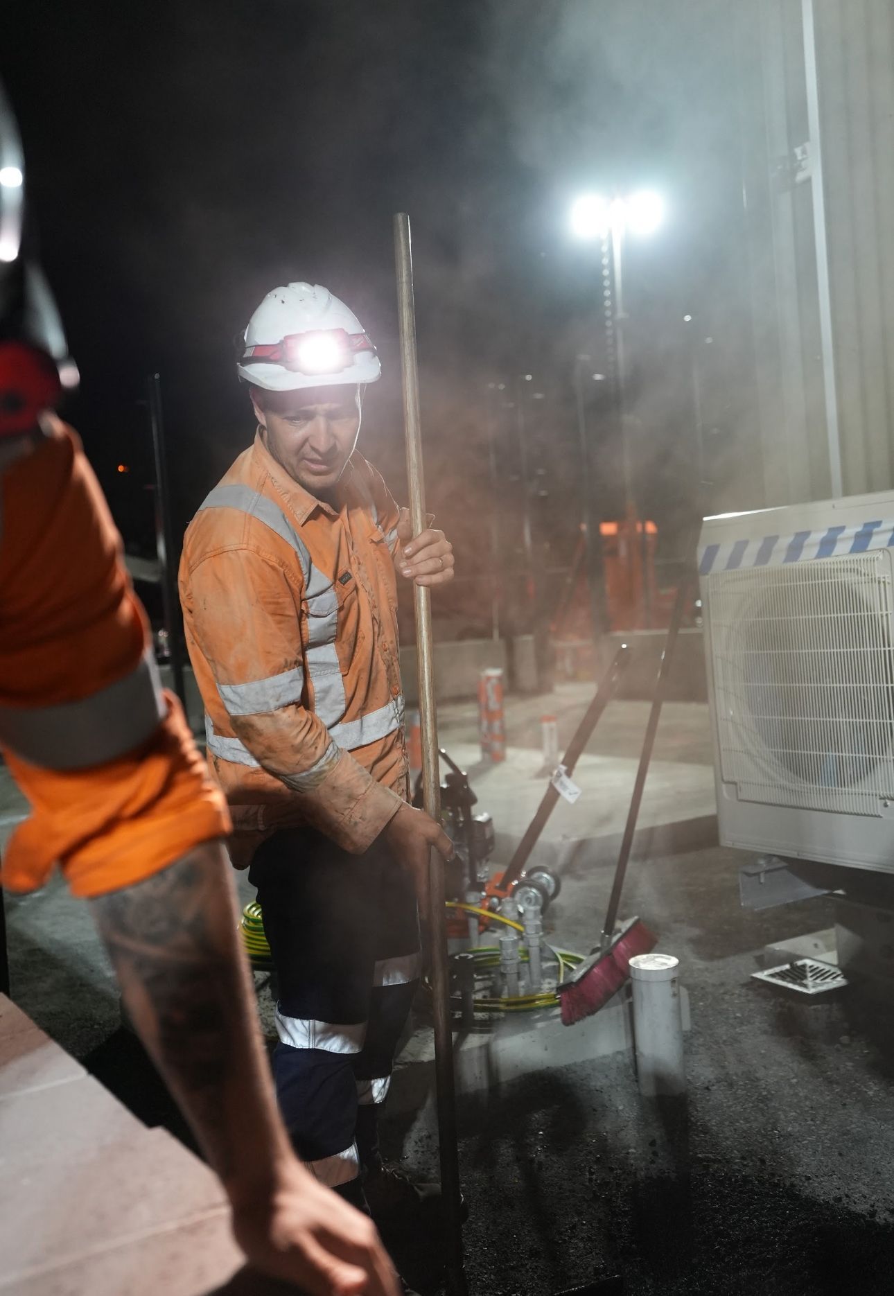 Construction worker with headlamp, operating equipment, outside at night.