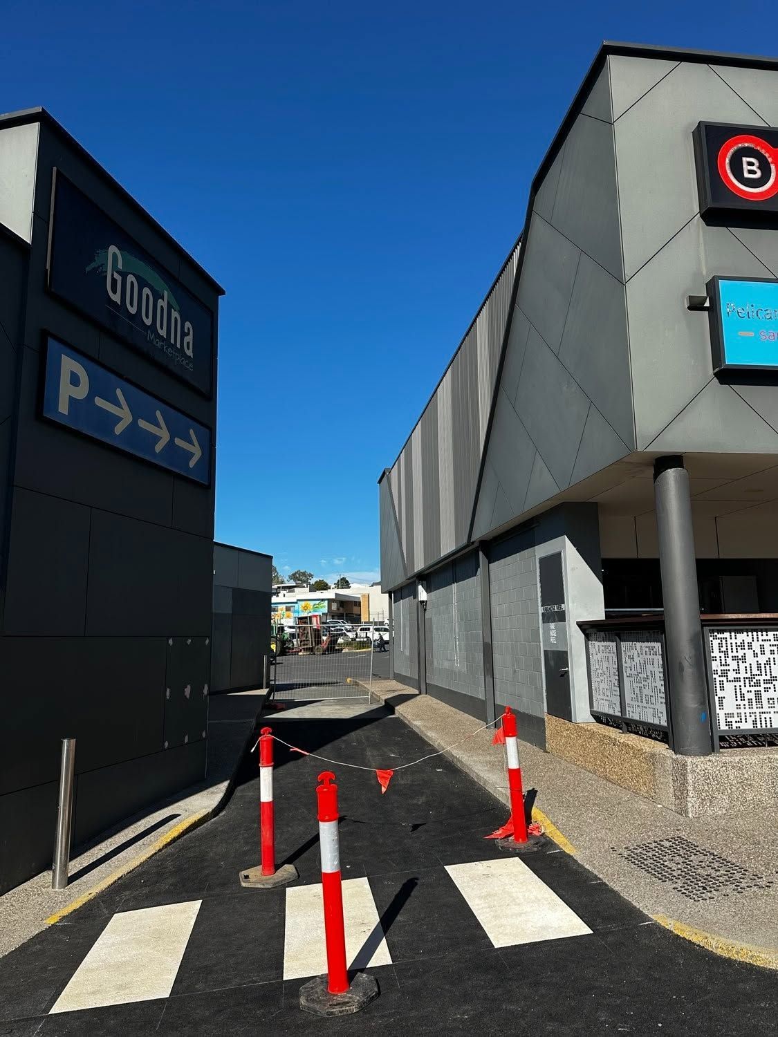 Narrow alley between dark buildings with crosswalk stripes and orange cones under a bright blue sky
