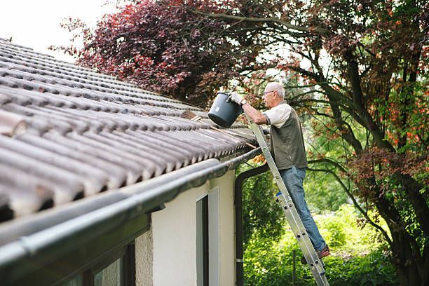 Man standing on a ladder to clean gutters on a tiled roof