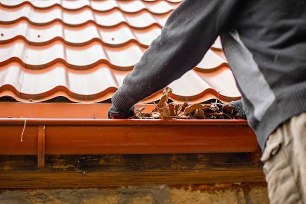 Gloved hand scooping dry leaves out of an orange roof gutter