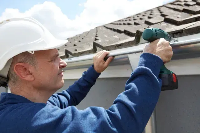 Roofer using a cordless drill to install seamless metal gutters
