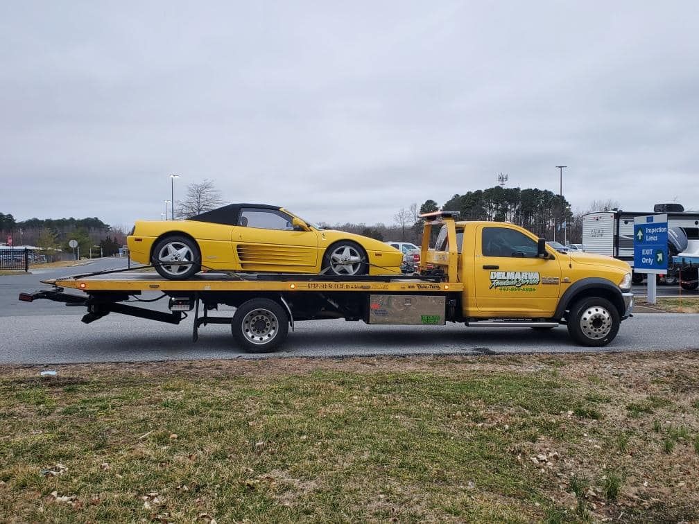 Yellow sports car on a tow truck parked beside a wet road under cloudy skies