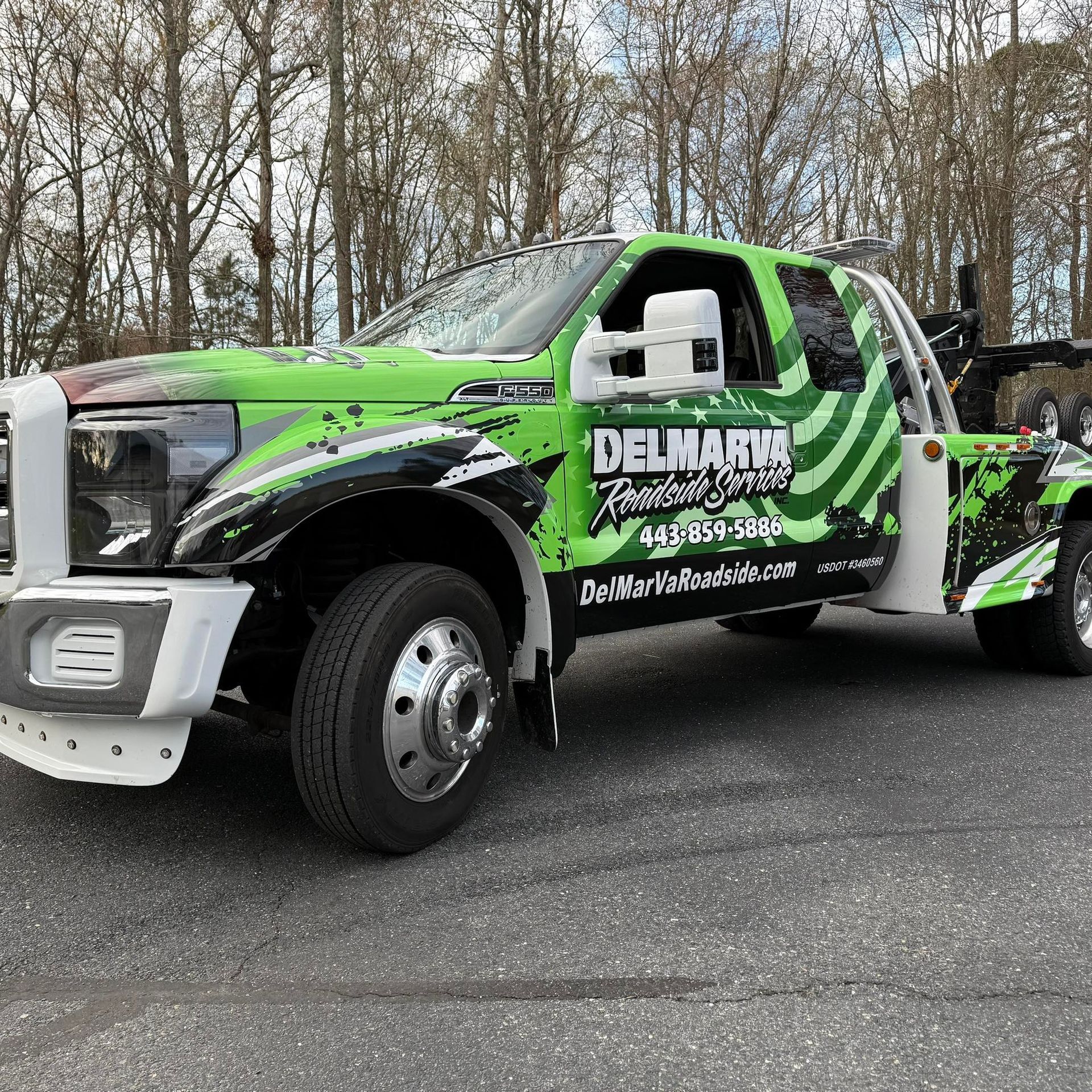 Green custom tow truck with black graphics parked on a road beside bare trees.