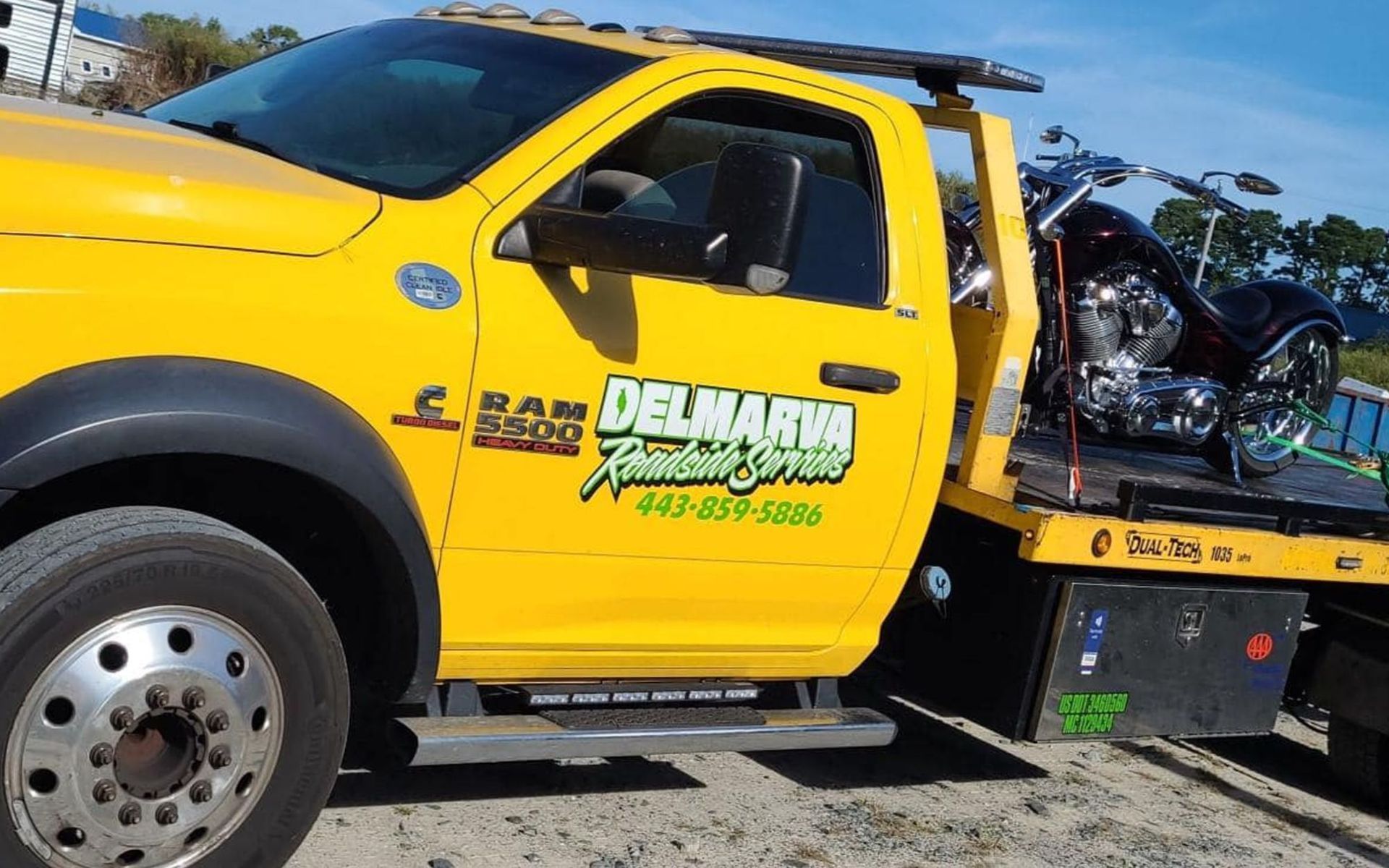 Yellow tow truck with a bike on the flatbed, parked outdoors under a blue sky.