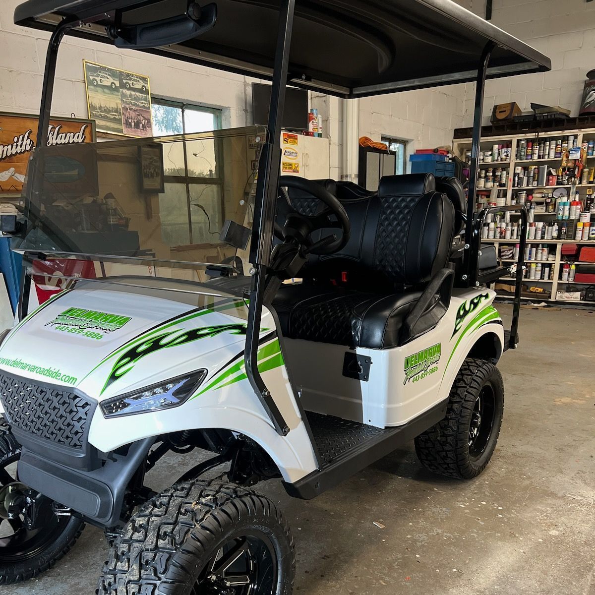 White and green golf cart in a garage, with black seats and off-road tires