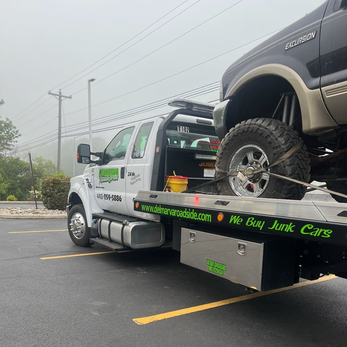Tow truck hauling a lifted black SUV on a wet road in foggy weather
