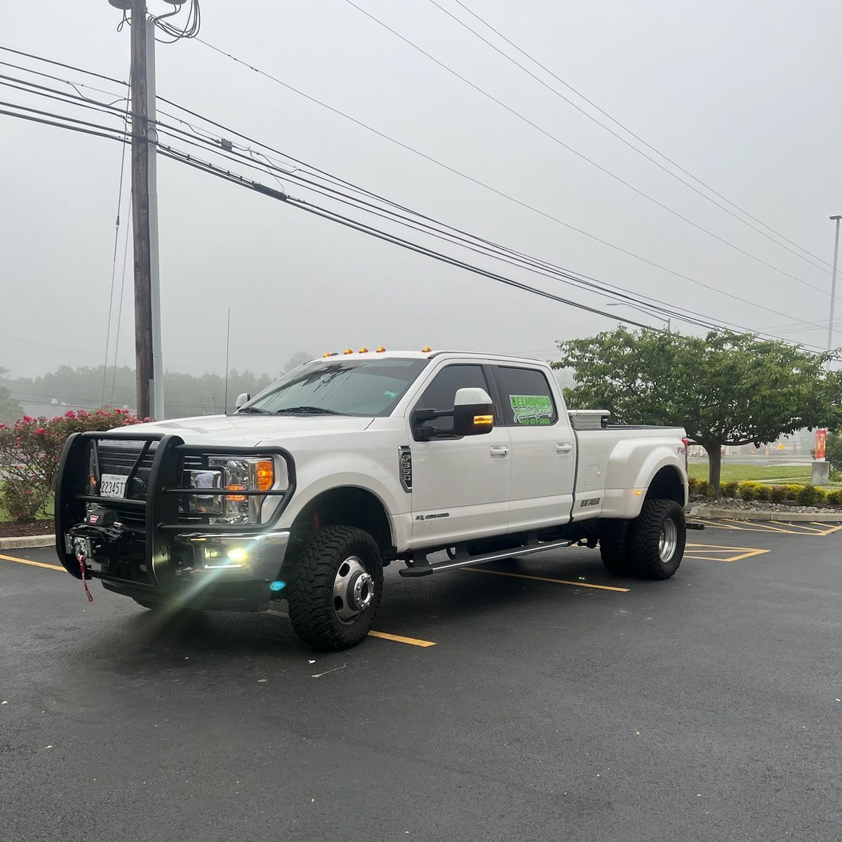White pickup truck with black grille guard parked in a rainy lot, power lines and trees in the background