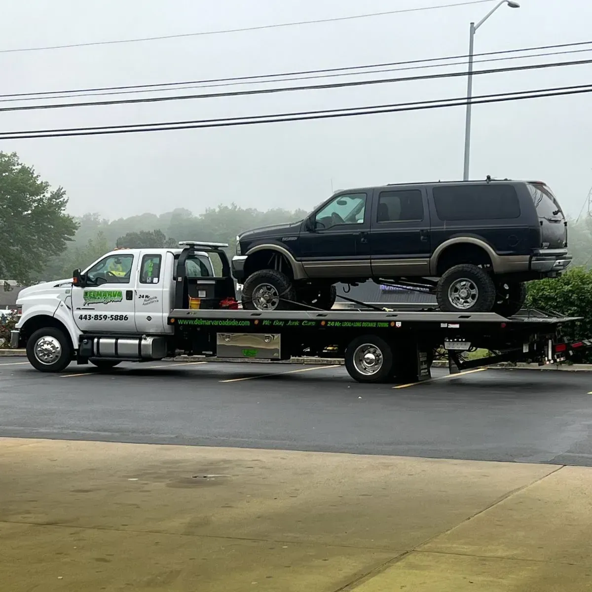 Tow truck carrying a black SUV on a flatbed in rainy roadside scene