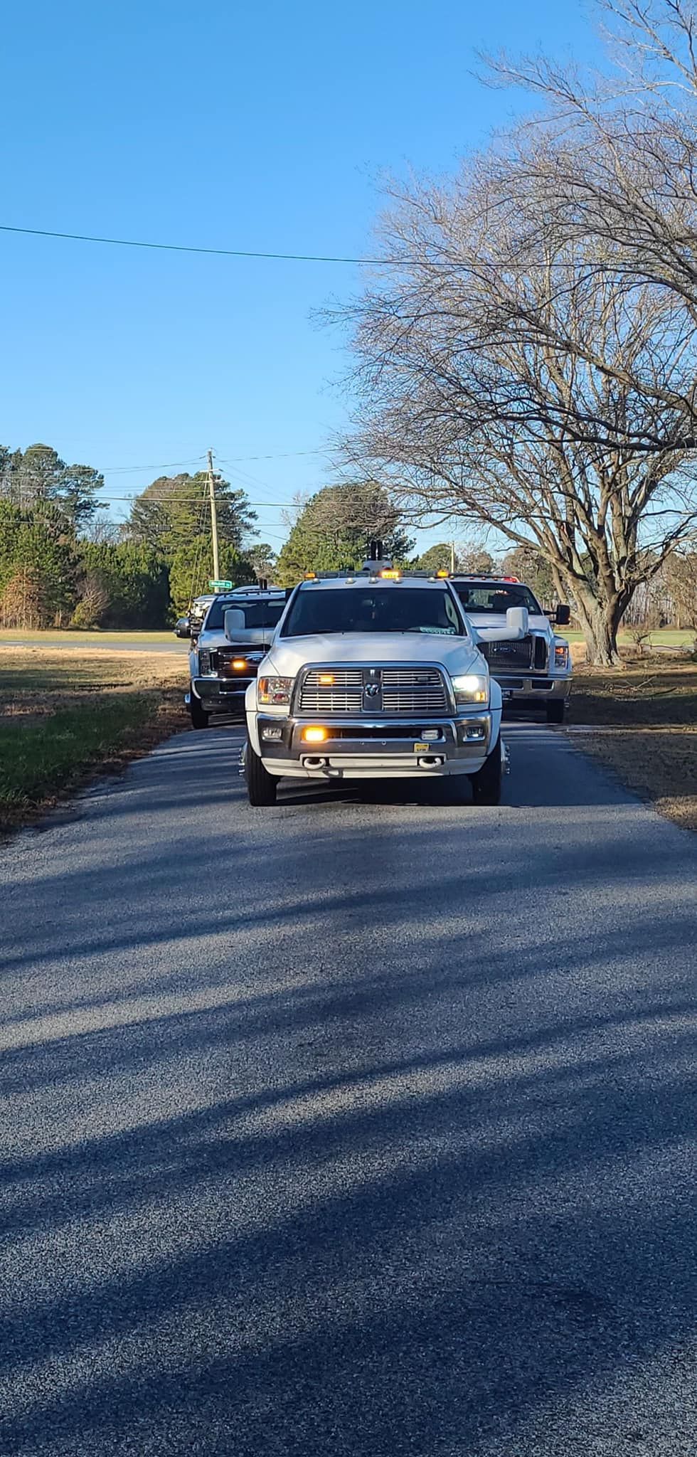 Silver SUV driving on a tree-lined gravel road under a clear blue sky