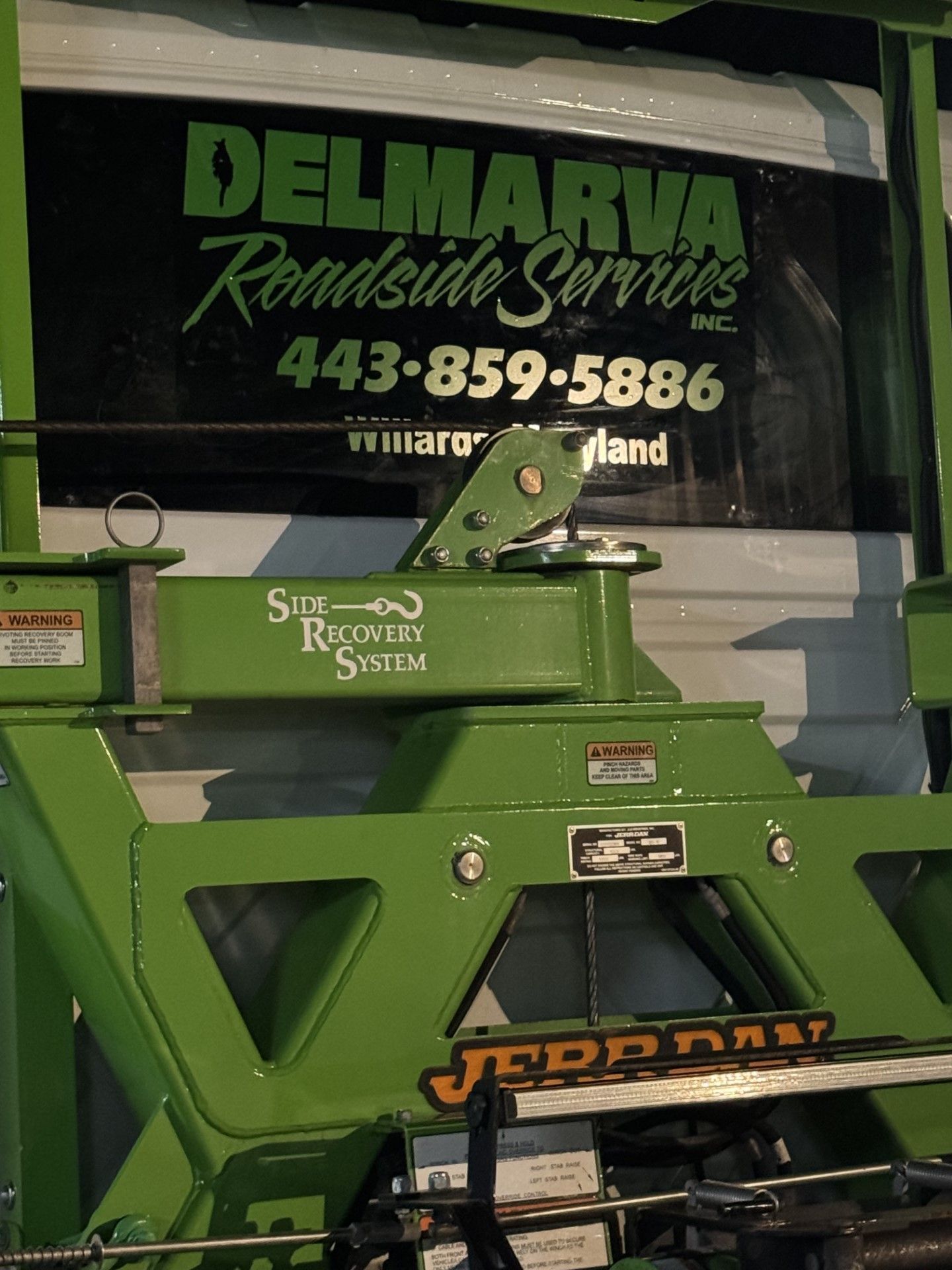 Green Delmarva Roads & Services machinery with “Jerr-Dan” logo, parked before a company truck window sign