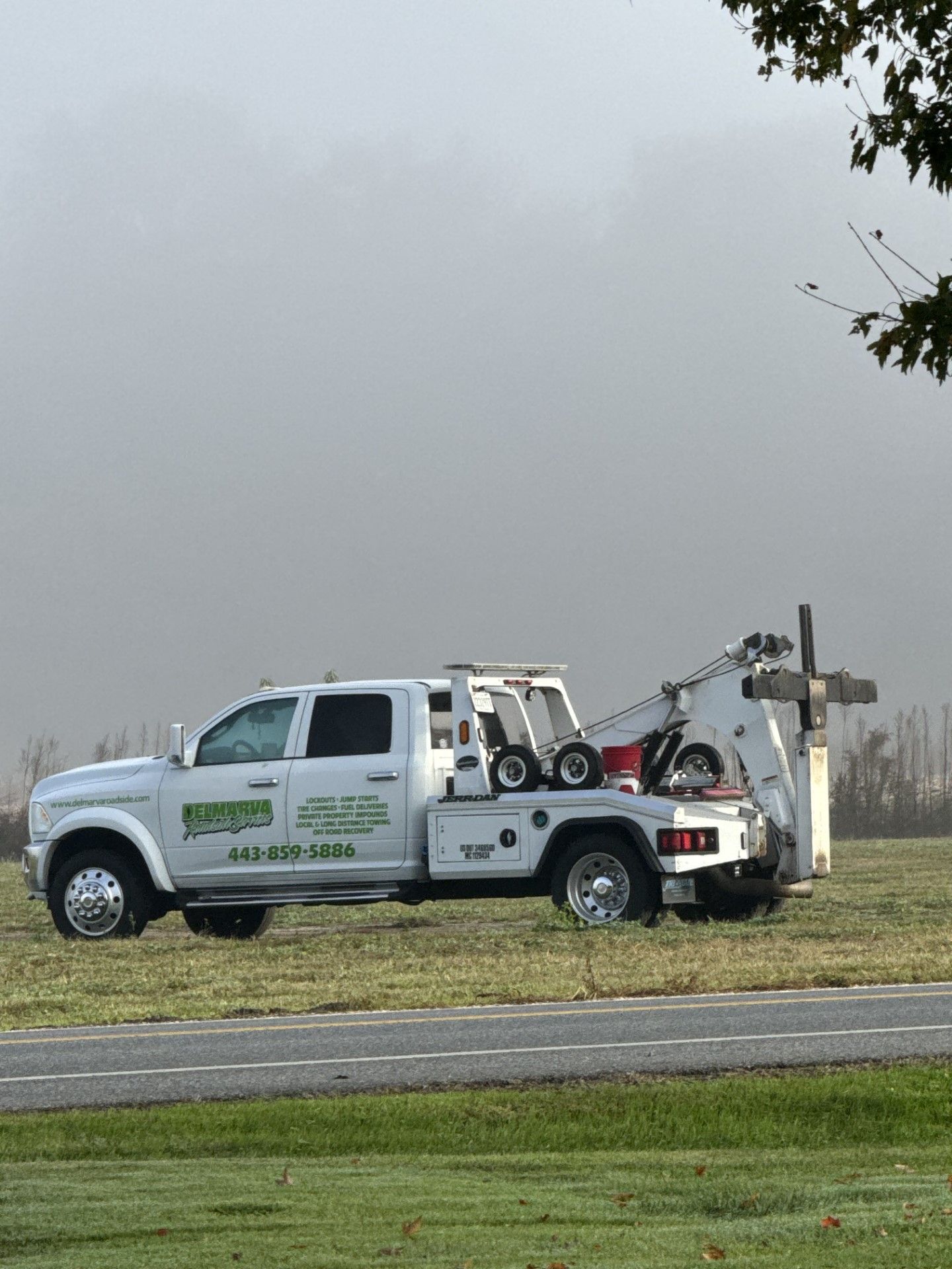 White tow truck with a car carrier on a roadside in a foggy field