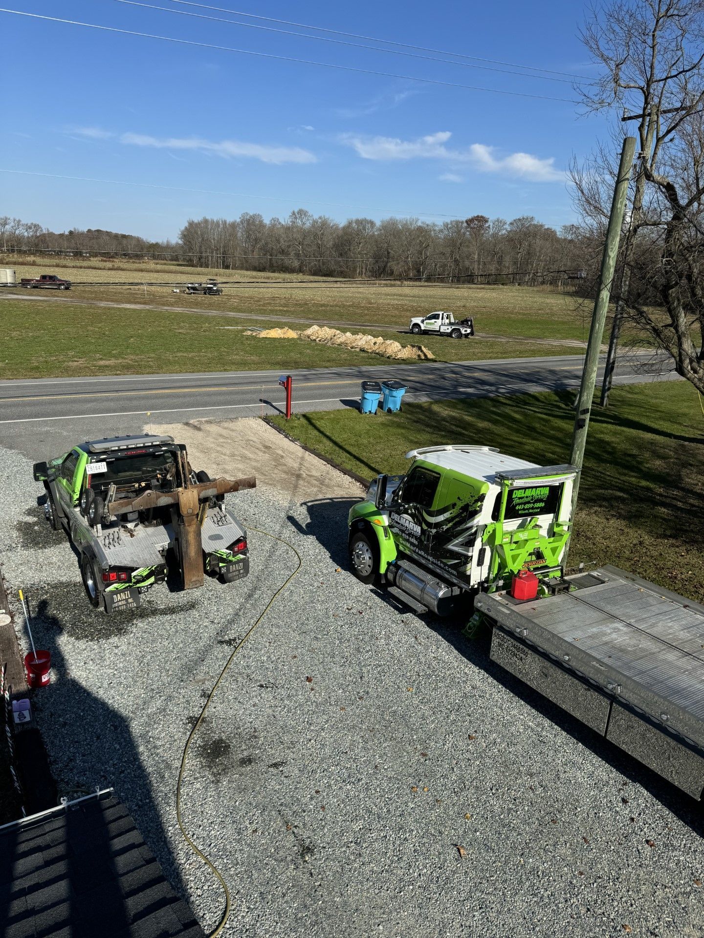 Two utility vehicles parked on gravel beside a grassy field under a blue sky