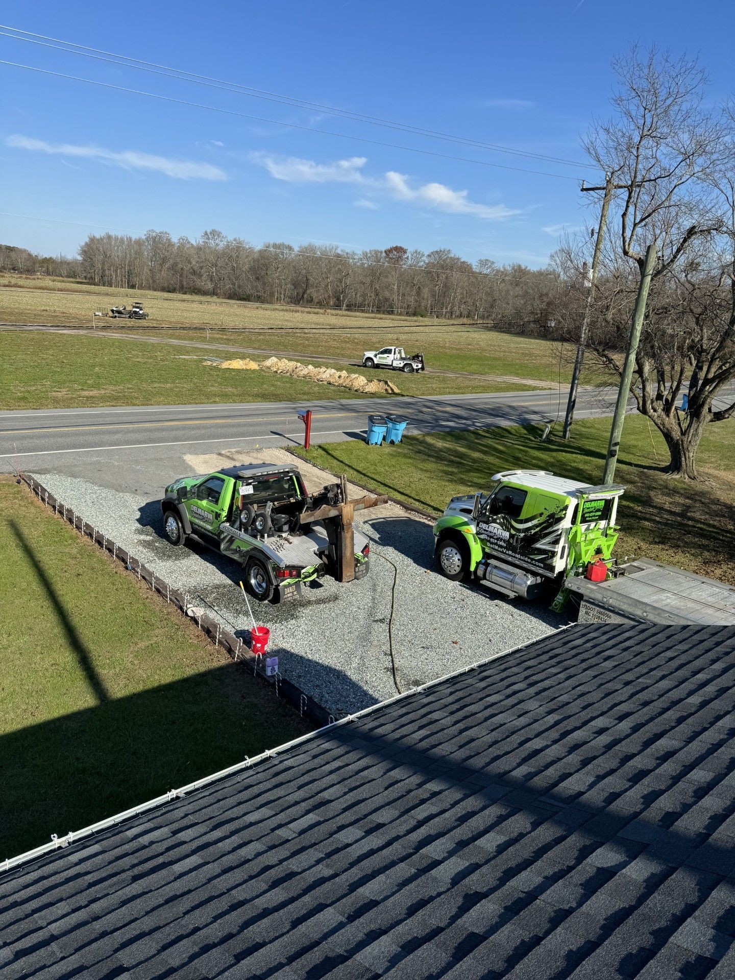 Two green utility trucks on a gravel driveway beside a house under a sunny blue sky