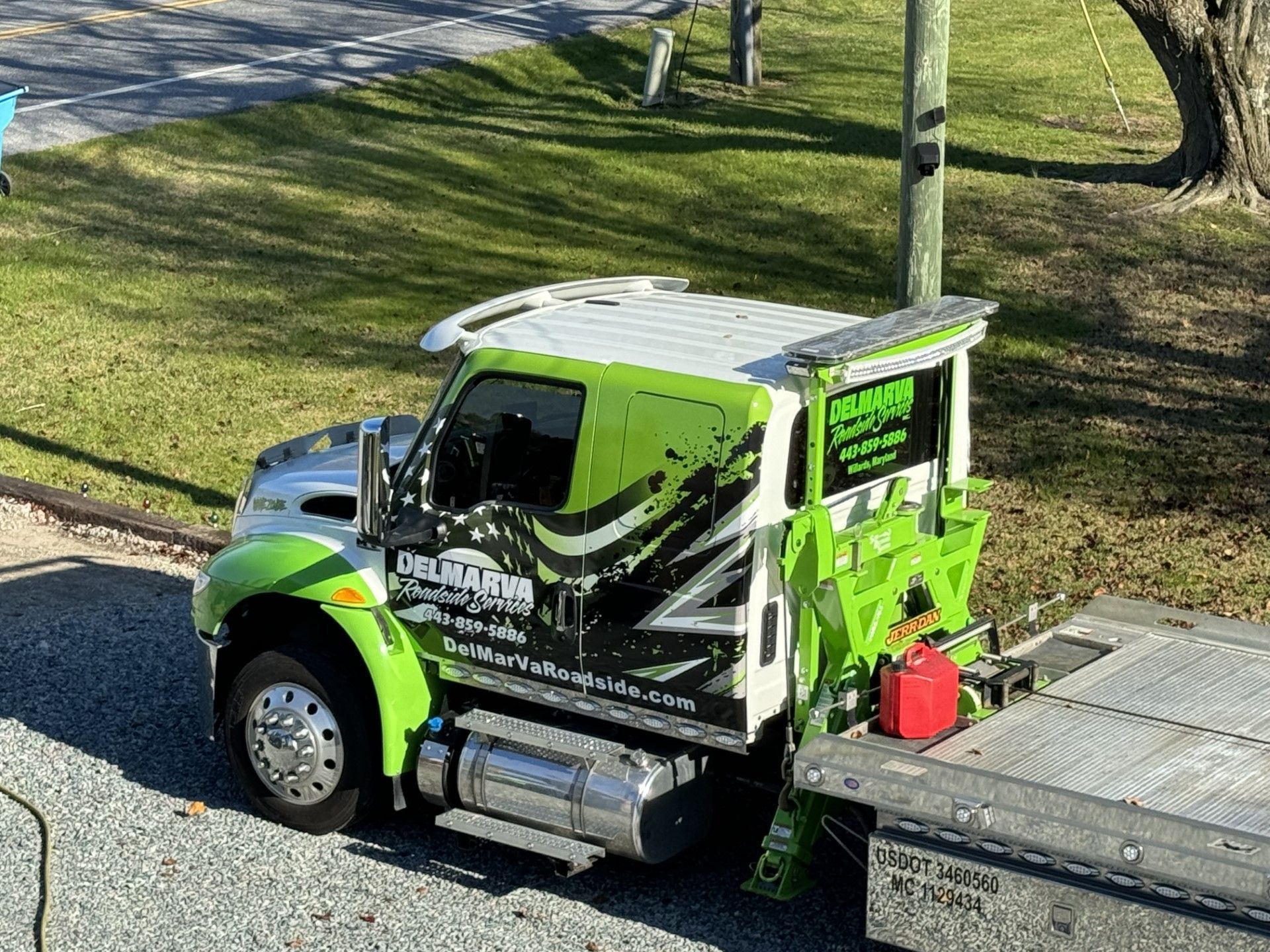 Green-and-black tow truck parked beside a flatbed trailer on a roadside.