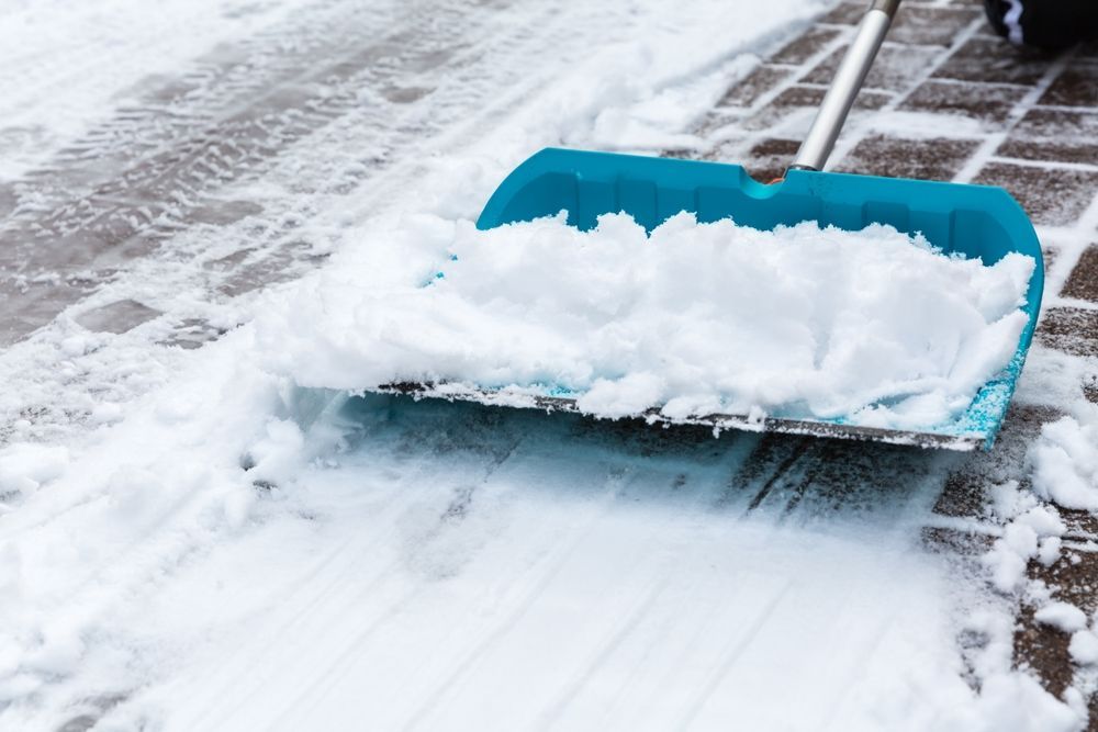 Blue snow shovel pushing snow across a snowy driveway