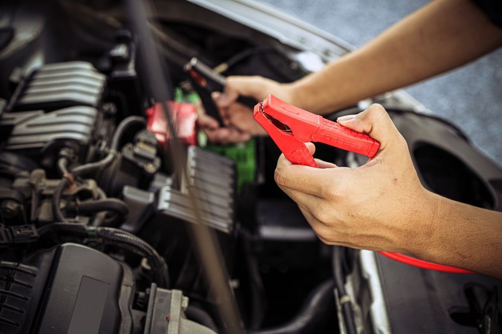 Hands using red jumper cables to connect a car battery in an engine compartment