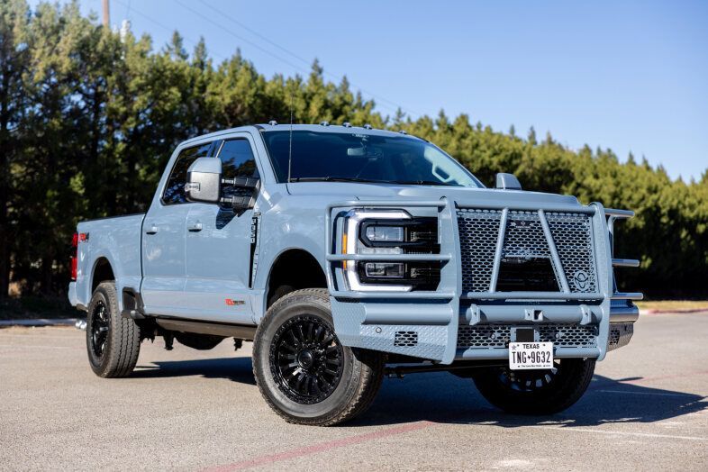 A blue truck is parked in a parking lot with trees in the background.
