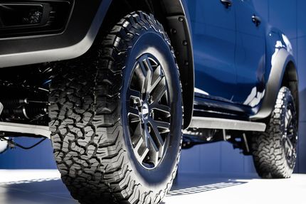 A blue truck with black wheels and tires is parked in front of a blue wall.