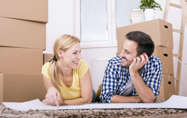 Man and woman smile AT EACH OTHER WITH BOXES BEHIND THEM.