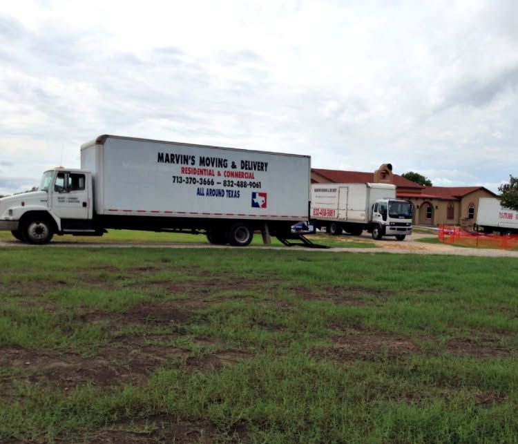 Moving truck with company logo parked on a grassy lot near a house under a cloudy sky.