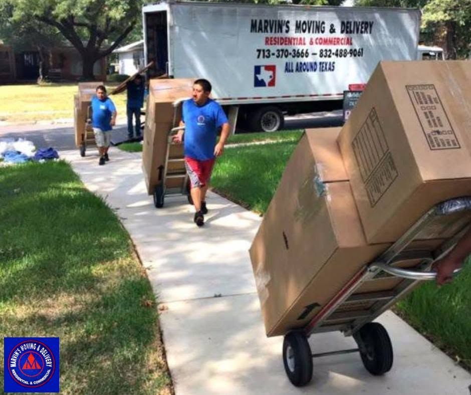 People moving boxes on dollies along a sidewalk beside a moving truck.