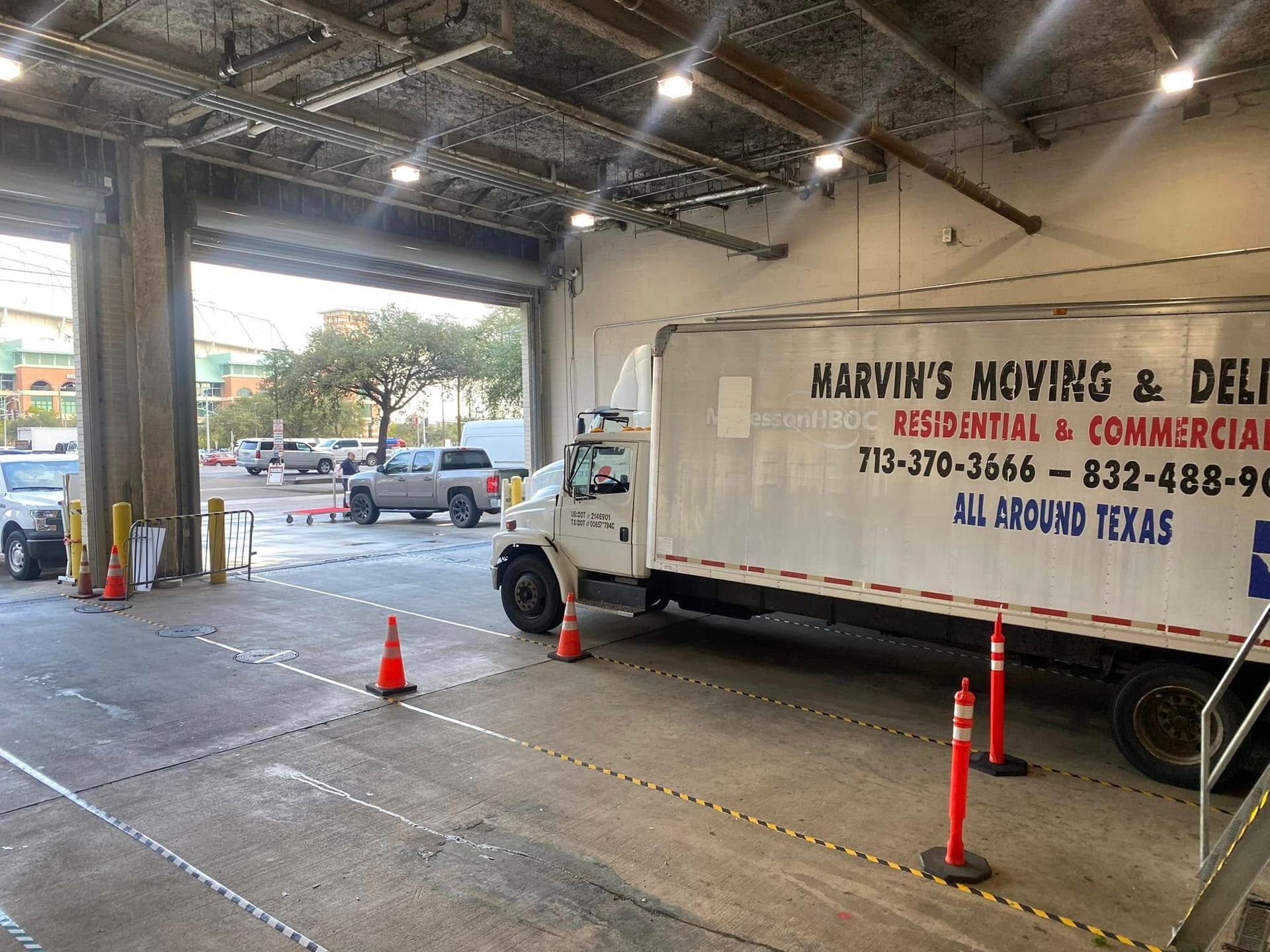 Moving truck at a covered loading dock, with orange cones and a red carpet on the concrete floor.