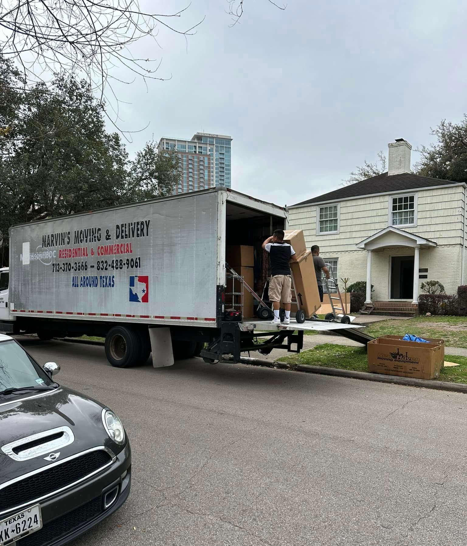 Moving truck unloading boxes outside a white house on a residential street