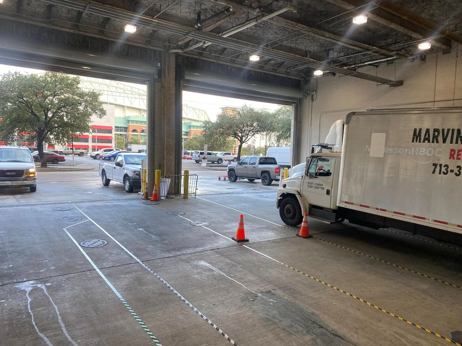 Warehouse loading dock with a white delivery truck, orange cone, and parked cars outside