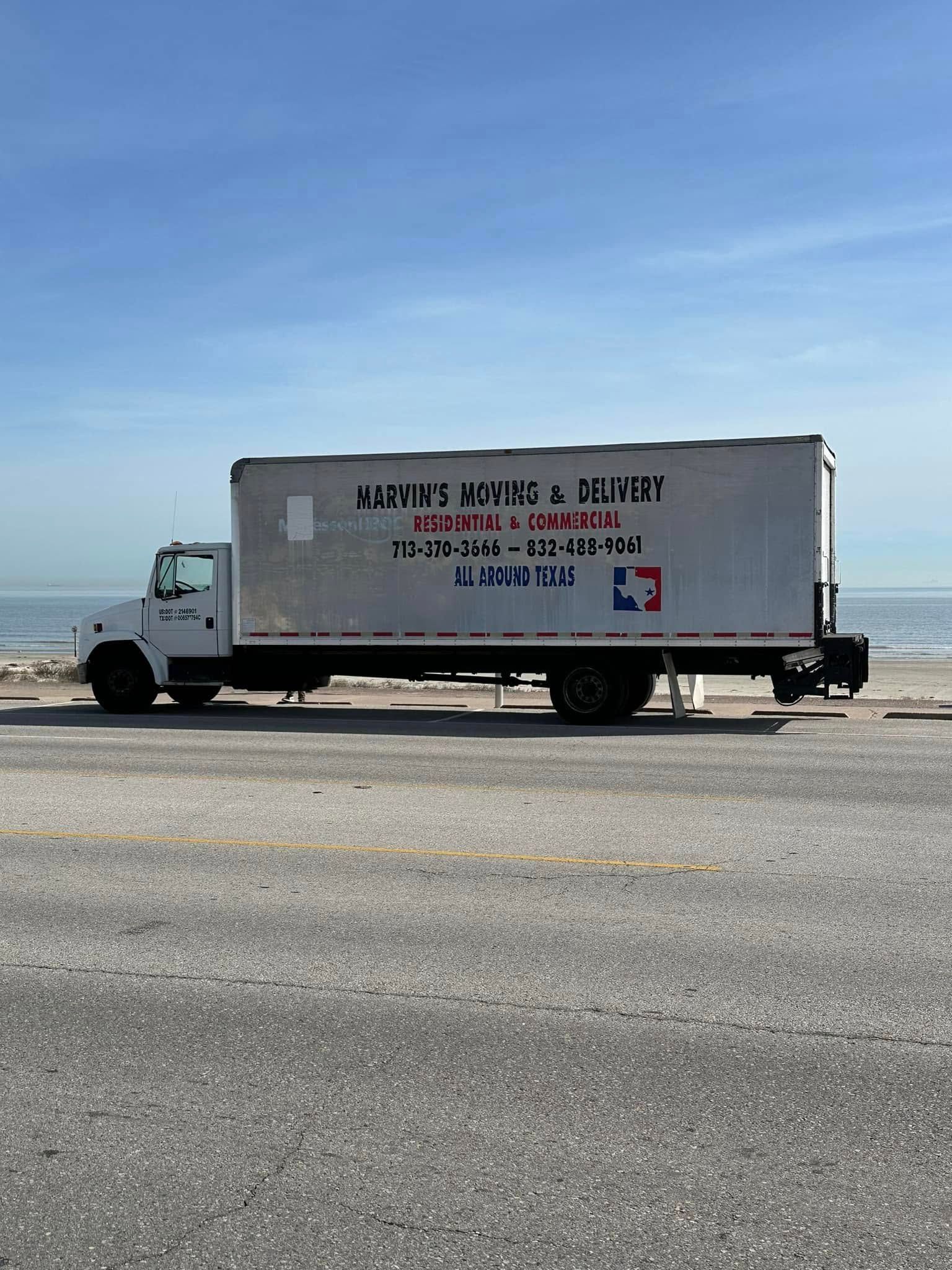 White box truck parked on a roadside by the ocean under a clear blue sky.