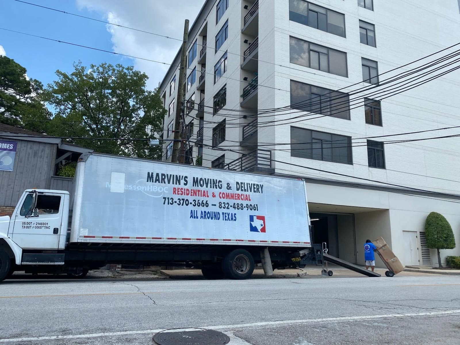 Moving truck parked beside a white apartment building on a city street