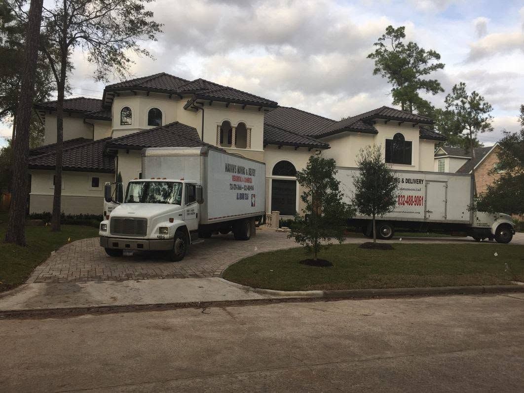 Large white moving truck parked in front of a two-story stucco house on a cloudy day.
