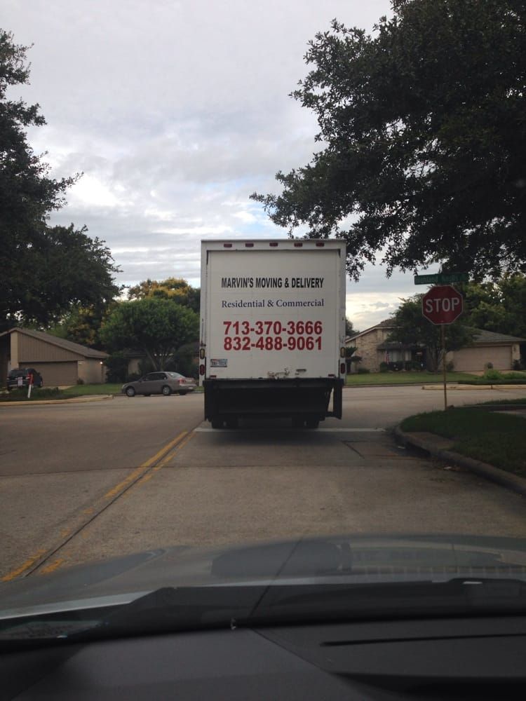 White moving truck ahead on a suburban street, with phone numbers on the back.