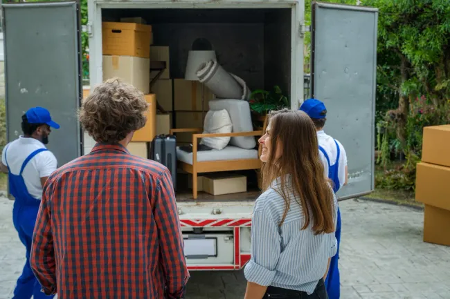 People loading boxed equipment into a shipping container with two workers nearby