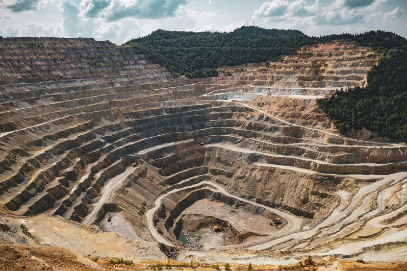 Terraced open-pit mine with stepped rock layers and exposed earth under a cloudy sky