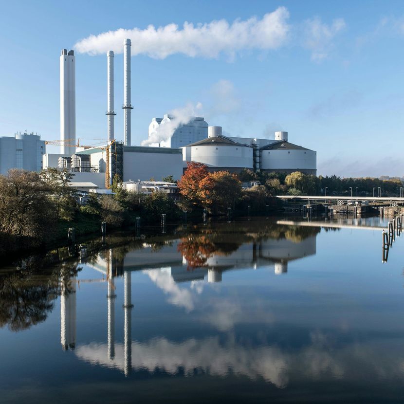 Industrial power plant with tall smokestacks reflected in a calm river under a blue sky