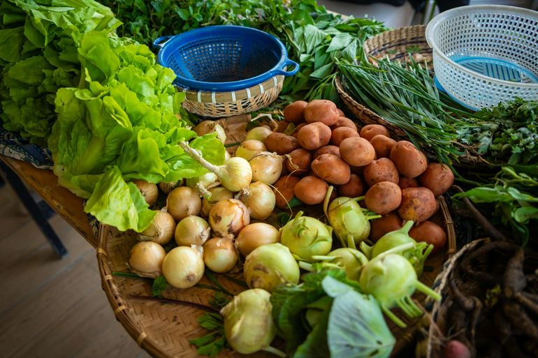 Fresh vegetables and onions displayed on a market table with baskets and leafy greens