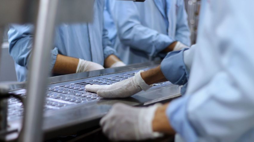 Gloved workers in blue coats handling packaged food on a production line