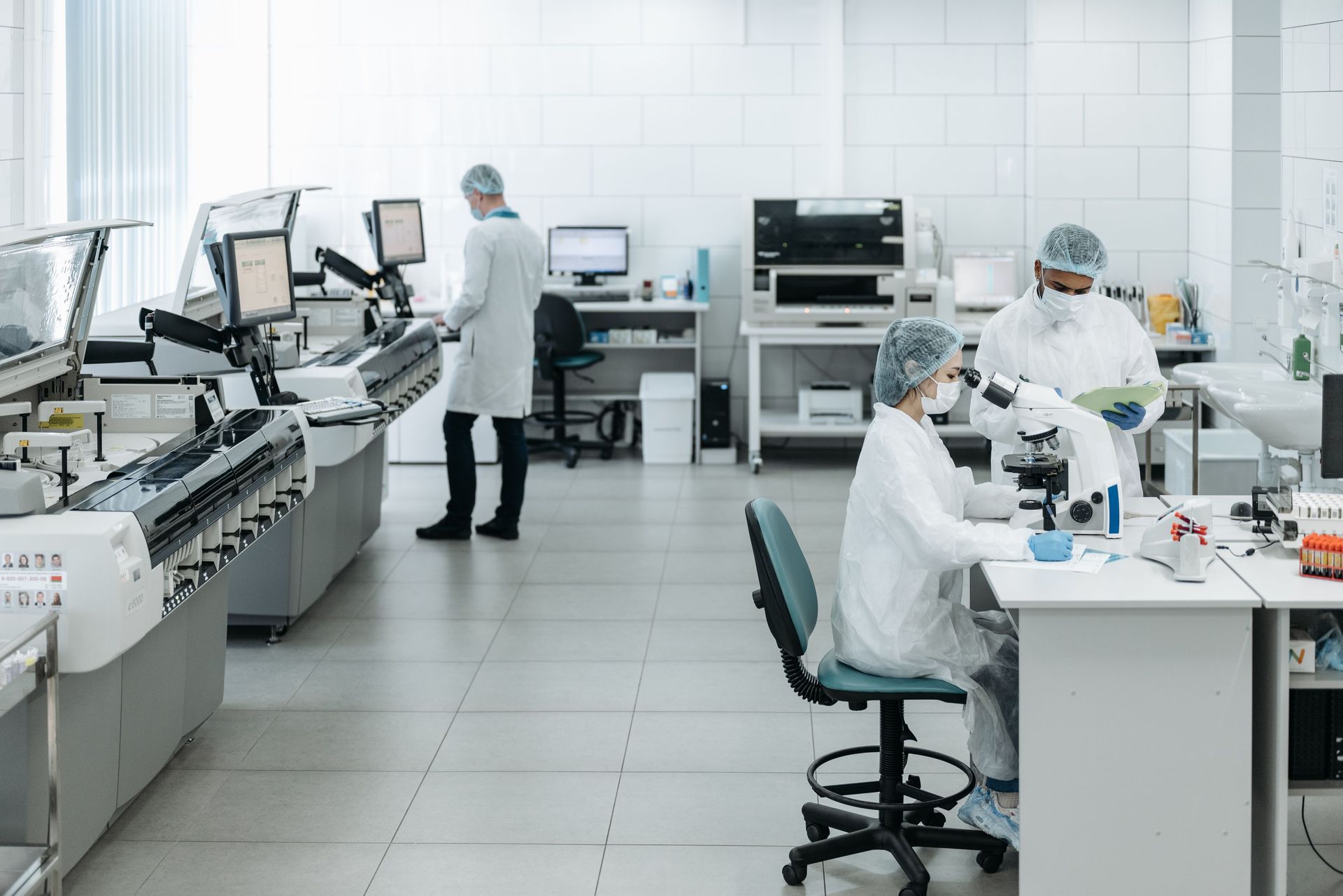 Bright laboratory with technicians in white coats working at microscopes and analyzers