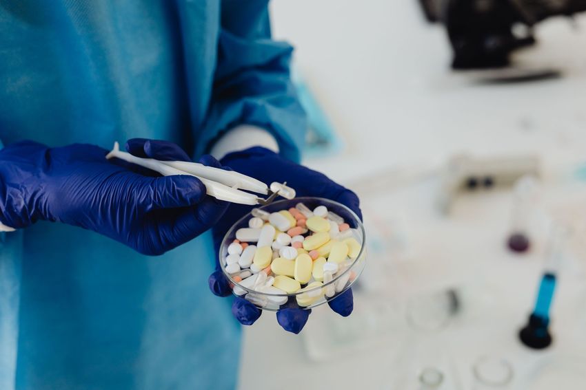 Gloved hands holding a petri dish with assorted pills in a lab setting