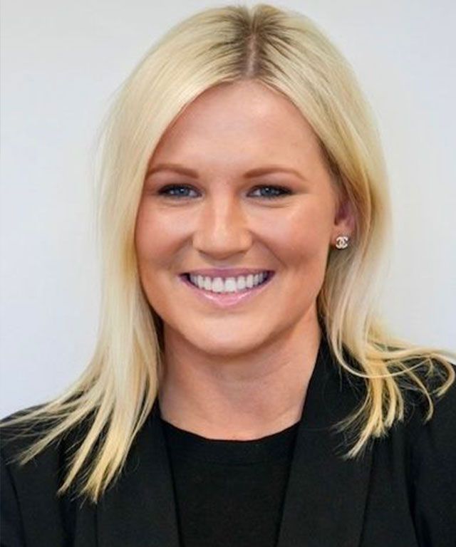 Woman with blonde hair smiling, wearing a black blazer, against a white backdrop.