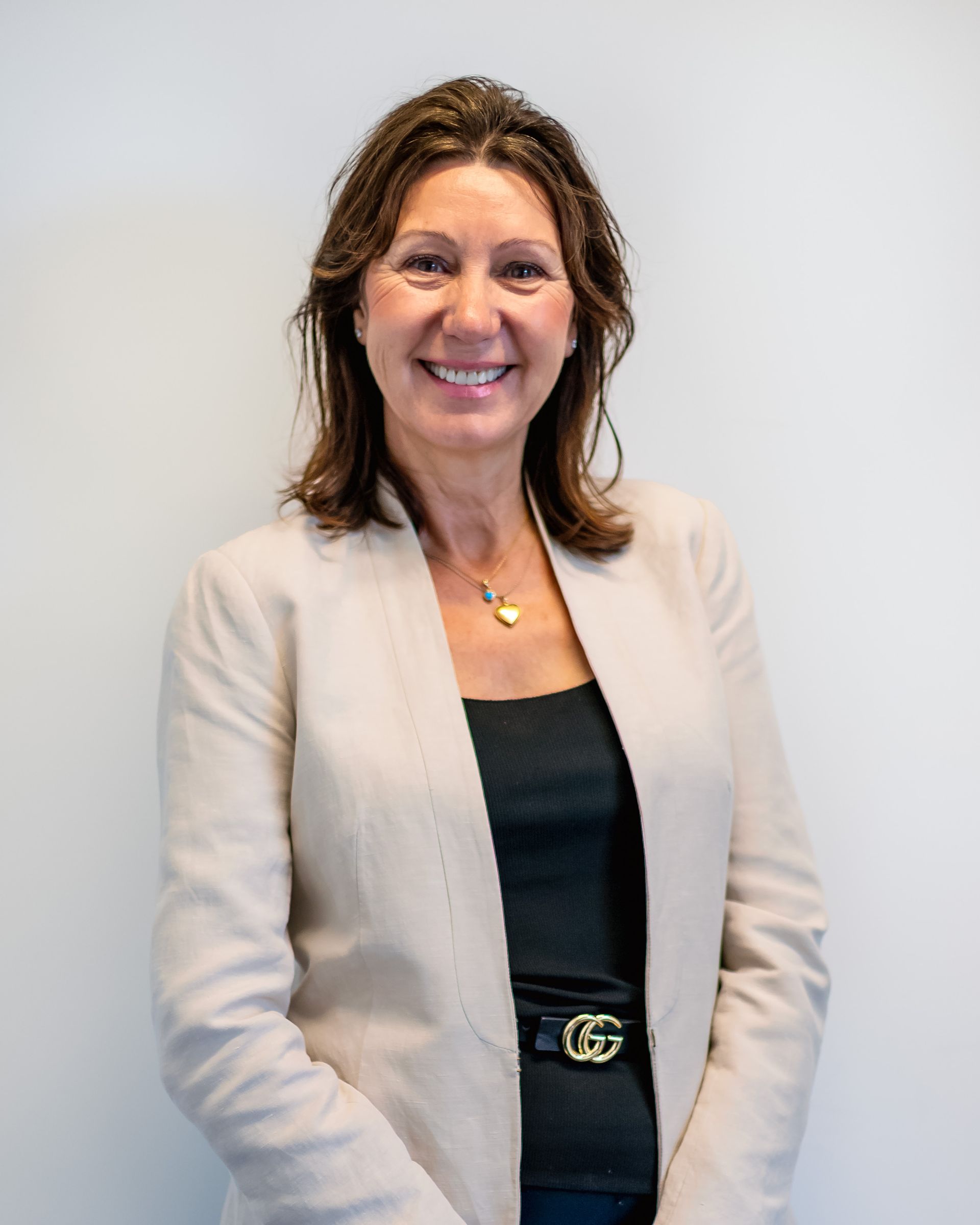 Woman in a blazer and black top smiles at the camera against a plain background.