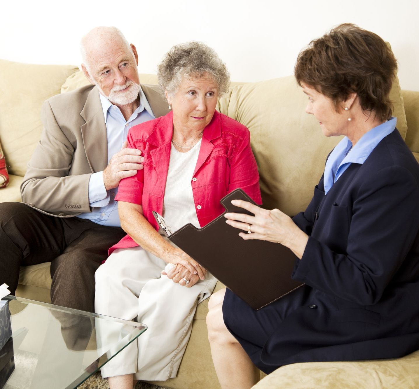 Senior couple with advisor discussing documents on a couch in a living room.