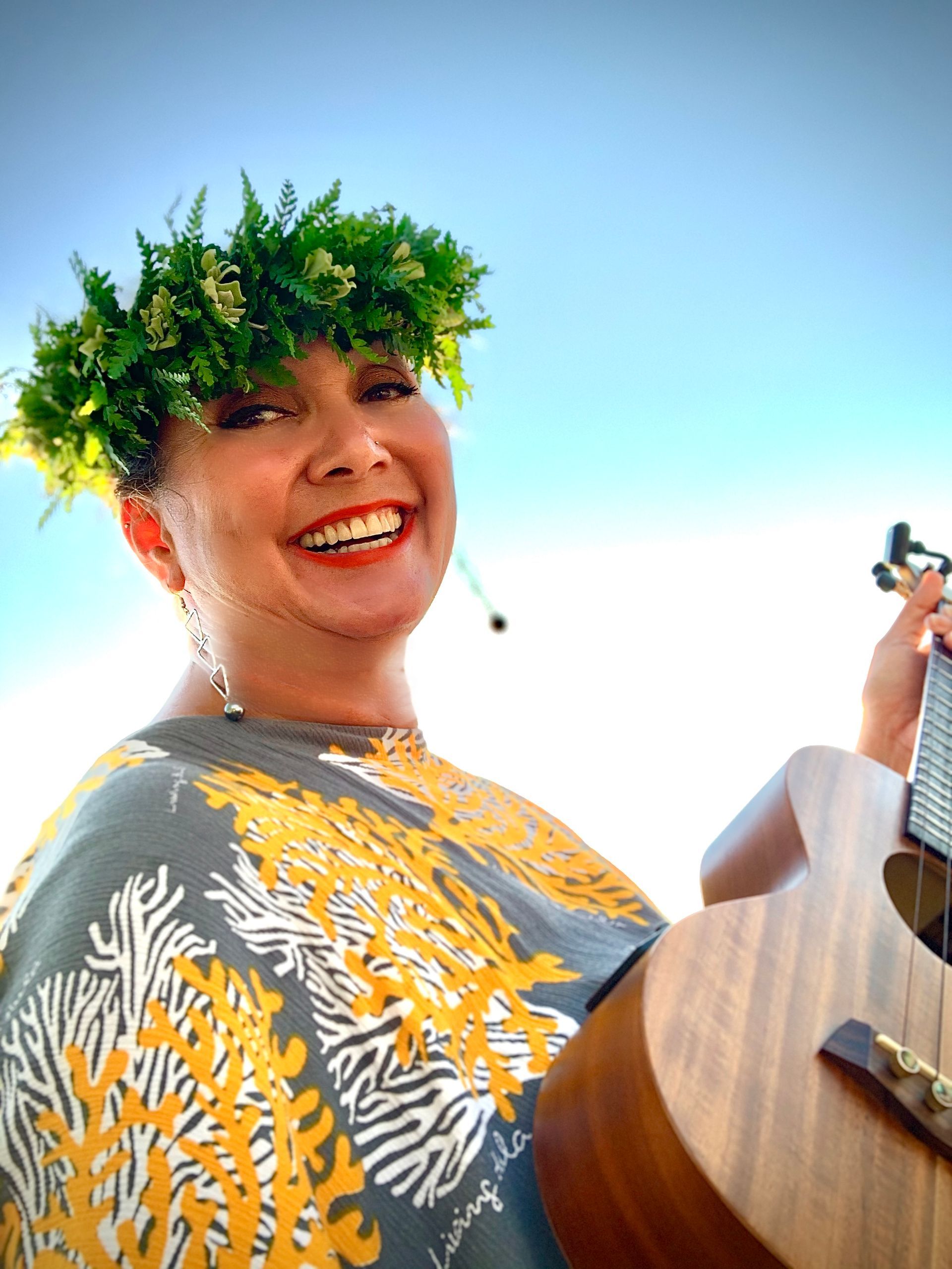 A woman wearing a lei is holding a guitar and smiling