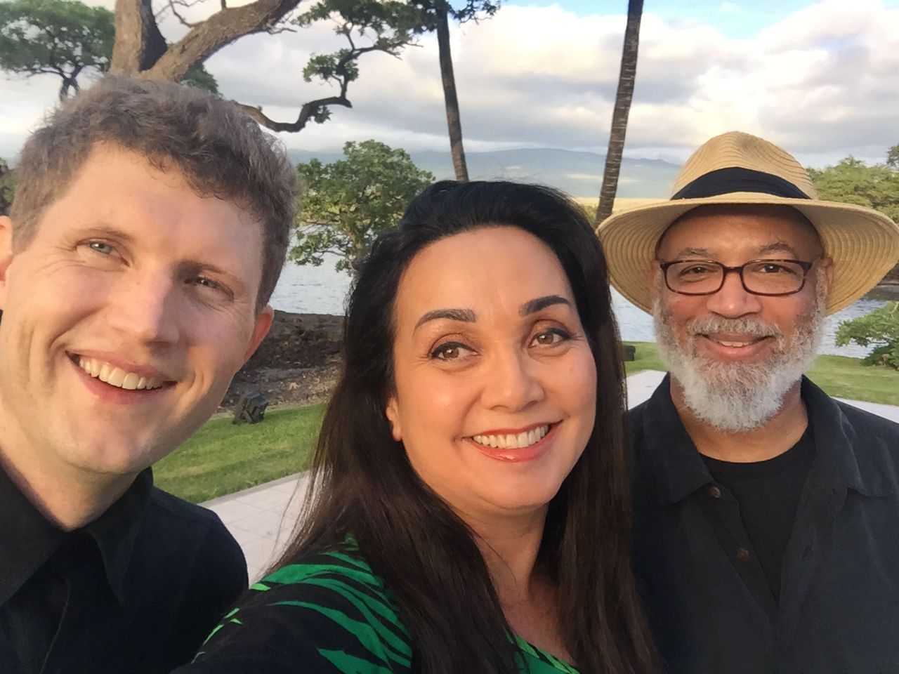 A man and a woman are posing for a picture with a man wearing a hat.